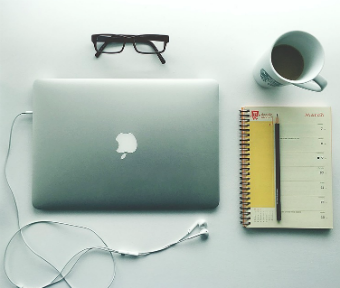Apple laptop with pair of glasses, coffee, and notepad