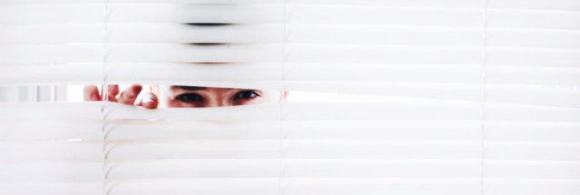 a woman peeking behind a white curtain blinds